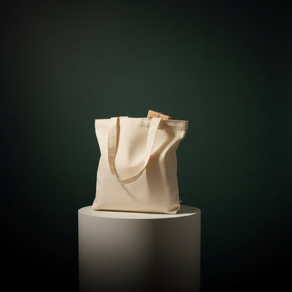 ONE1DUB natural cotton canvas tote bag with reinforced handles, shown with a woman placing a small gift inside.